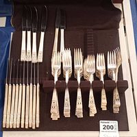 Set of knives, forks, and steak knives silverplated with detailed embossed handles, arranged in a brown flatware case.