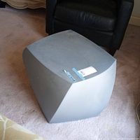 Gray left twist cube end table shown from an angled top view, placed on carpet with a black chair in background.