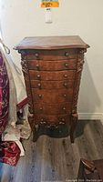 Front view of the floor standing jewelry chest showing carved details and six drawers with metal knobs.