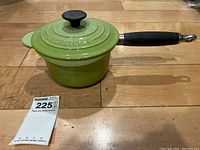 Green Le Creuset saucepan with lid and black handle on wooden surface.
