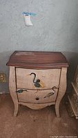 Front view showing curved-front two-drawer nightstand with painted birds and distressed finish.