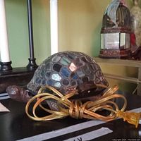 Front-side angle view of the turtle lamp displaying the mosaic stained glass shell and metal head and legs, along with the attached power cord.