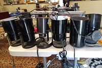 Front view showing six black metal uplight spotlight lamps on a table with power cords and adjustable heads.