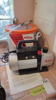 Photo showing Robinair VacuMaster vacuum pump sitting next to a vacuum container with an orange rim, gauge, and hose setup.