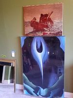 Photo showing two art prints stacked against a green wall. The top print depicts fishermen in a boat in warm tones; the bottom print shows an abstract shape in blue and black.