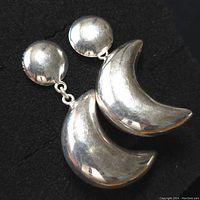 Pair of sterling silver earrings on black background showing crescent moon dangle and round stud attachment.