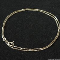 Sterling silver chain necklace laid in circular shape on black background showing chain details and clasp.