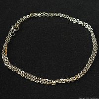 Photo of the full silver chain necklace laid out in a circle on a black surface, showing the chain links and clasp.