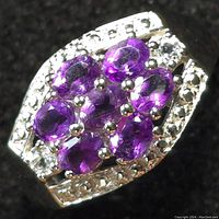 Close-up photo of silver ring with seven oval amethyst stones and surrounding white topaz stones on a polished silver band.