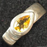 Close-up photo of sterling silver ring with pear-shaped yellow gemstone on a black background showing stone and band details.
