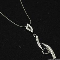 Close-up image of silver necklace with cubic zirconia embedded pendant on a black fabric background for contrast.