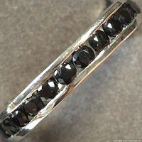 Close-up photo of silver ring with black onyx stones set around the band, showing faceted surface of stones and polished silver.