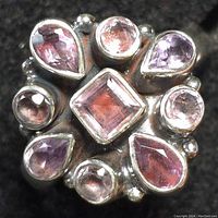 Close-up photo of the silver ring showing eight faceted amethyst stones in pear, round, and square cuts arranged in a floral pattern.