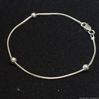 Sterling silver bracelet displayed on black background, showing the thin snake chain, three round bead accents, and lobster clasp closure.
