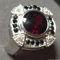 Close-up front view of silver garnet ring showing large round faceted garnet and surrounding black and clear stones