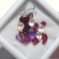 Multiple assorted genuine gemstones of various shapes and colors on white background in small tray.