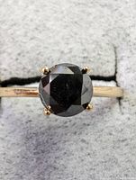 Close up photo of ring face showing large round black diamond in four-prong 10k yellow gold setting