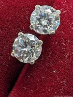 Close-up image of a pair of 14k gold moissanite stud earrings on a red velvet background showing the round cut of the stones and 4-prong settings.