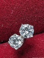 Two stud earrings on red velvet background.