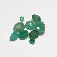 Top-down photo of nine loose emerald gemstones of various shapes and sizes showing color and condition.