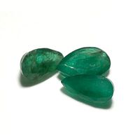 Photo showing three pear-shaped green emerald gemstones on a white background with natural inclusions visible.