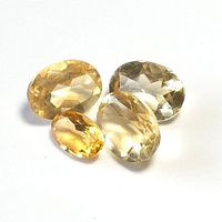 Four oval cut citrine gemstones displayed on a white background, showing transparency and faceted surfaces in pale yellow to golden hues.