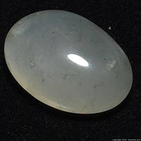 Close-up photo of oval polished moonstone showing translucency and light reflection.