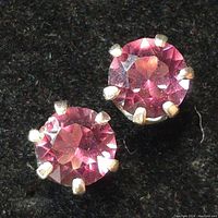 Close-up photo of silver stud earring with round faceted pink gemstone set with four prongs against black background