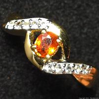 Close-up photo of the sterling silver ring with oval orange sapphire center stone and clear accent stones on band taken from an angle showing details of setting and stones.