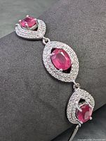Close-up of bracelet showing pinkish-red oval ruby stone with halo of small clear stones on sterling silver setting