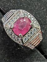 Close-up of ring showing oval cut ruby center and surrounding cubic zirconia stones on sterling silver band.