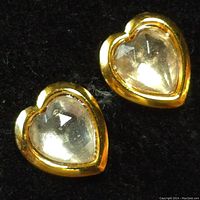 Close-up photo of one heart-shaped earring showing clear faceted center stone with gold-tone bezel setting