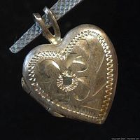 Front view of heart-shaped pendant locket showing embossed floral design and bail.