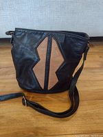 Front view showing black leather purse with front brown geometric leather design and shoulder strap.