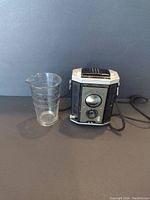 Side by side photo of the camera and glass measuring cup on black background to show scale and condition.