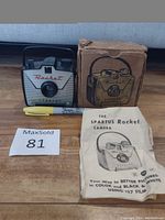 Antique Spartus Rocket camera with original box, instruction leaflet, and MaxSold tag on wooden surface.