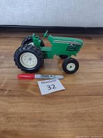 Side view of green ERTL tractor die-cast model with white wheels and large rear tires next to a red Sharpie marker for scale.