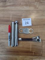 Top view showing three cylindrical stainless steel parts of the flask disassembled, a stainless steel cigar cutter with two finger holes, and a metal holder.