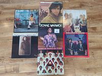 Seven LP vinyl records laid out on wood floor, album covers visible showing various artists and wear on sleeves