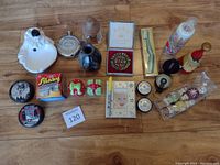 Photo of miscellaneous vintage and collectible items arranged on wooden floor, showing a variety of toy, decor, cosmetic, and collectible pieces.