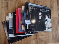 Seven LP albums stacked on wooden floor showing front covers with visible wear and varied artwork.