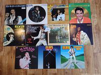 Photo showing all 11 Elvis Presley LP records arranged face-up on wooden floor. Each album has different cover art including concert photos, portraits, and colorful prints.