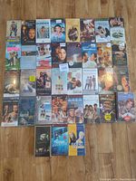 Lot of 37 sealed VHS movie tapes arranged in rows on a wooden floor showing their front cover art.