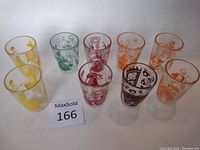 Nine small vintage Kraft juice glasses arranged in 3 rows with various cartoon prints in yellow, green, red, orange, and black.