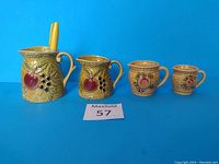 Set of four vintage ceramic measuring cups with fruit embossing on blue background.