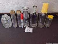 Overview of the eight vintage glass bottles and jars arranged in a row on a flat surface with a MaxSold lot number card visible
