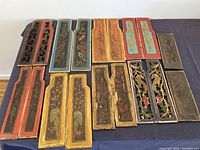 Full view of all 18 antique Chinese carved wood panels arranged on a fabric surface, showing various colors and carving styles.