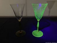 Two antique uranium glasses under UV light showing bright fluorescence of the green glass