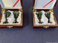 Two wooden boxes each holding two green jade cordial glasses nestled in white satin lining. Both boxes are open and visible from above.