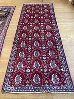 Full view of red Persian wool runner with floral and paisley motif and a decorative border on a wooden floor.